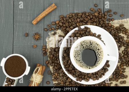 Tasse mit heißem Kaffee auf dem Hintergrund von Körnern und gemahlenem Kaffee. Blick von oben. Fertig, Bohnen und gemahlener Kaffee. Stockfoto