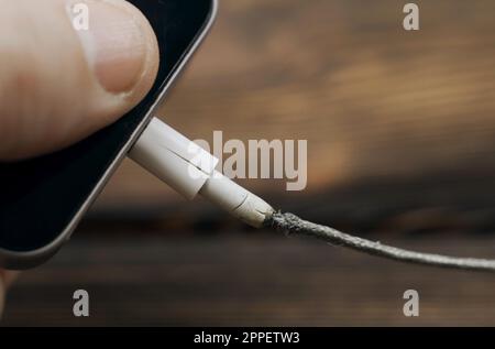 Trennen des defekten Telefons und Anschließen eines neuen Ladekabels. Gefahr, Brandschutz, Kurzschluss. Stockfoto