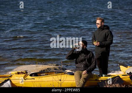 Männer in der Nähe von Kajaks an der felsigen Küste Stockfoto