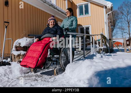Mutter macht Winterspaziergang mit Tochter im Rollstuhl Stockfoto