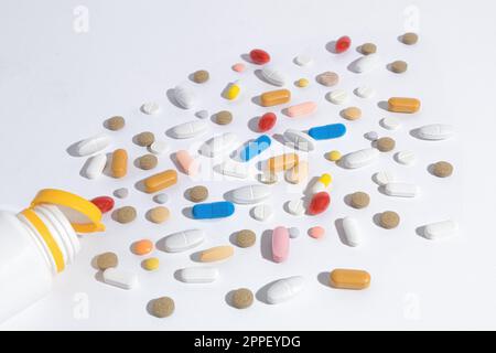 Viele Pillen auf dem Tisch, Nahaufnahme. Tabletten mit unterschiedlichen Formen und Farben sind auf dem Tisch verstreut. Die Pillen sind aus der Flasche gelaufen Stockfoto