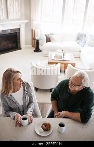 Nehmen Sie sich Zeit, um Zeit zu verbringen. Ein reifes Paar, das an einem entspannten Tag zu Hause Kaffee und einen Snack zusammen isst. Stockfoto