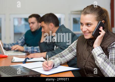 Eine Frau in einem karierten Hemd, die im Büro telefoniert Stockfoto