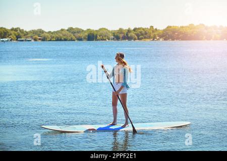 Schwimmt auf ruhigen Gewässern. Eine attraktive junge Frau, die auf einem See paddelt. Stockfoto
