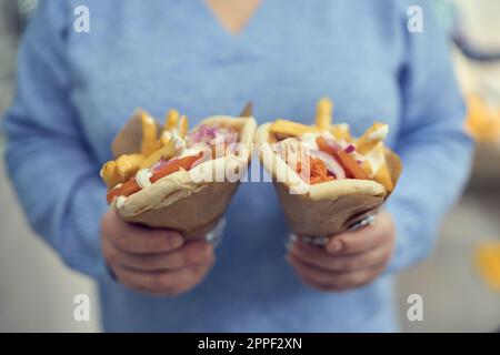 Unbekannte Frau, die zwei griechische Gyros-Sandwiches in der Hand hält. Eine Erwachsene Frau hält Pita Souvlaki-Snacks in einem Fast-Food-Restaurant Stockfoto