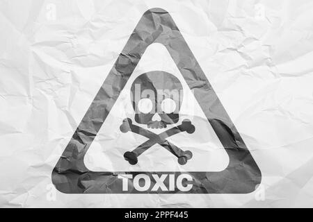 Warnschild (Schädel- und Kreuzknotensymbol und Wort „GIFTIG“) auf zerknittertem weißem Papier, Draufsicht Stockfoto