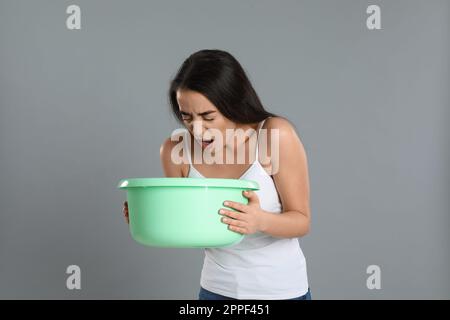 Junge Frau mit Becken mit Übelkeit auf grauem Hintergrund. Lebensmittelvergiftung Stockfoto