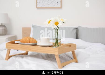 Blumenstrauß mit wunderschönen Gänseblümchen und Frühstück auf einem hölzernen Tablett im Schlafzimmer Stockfoto