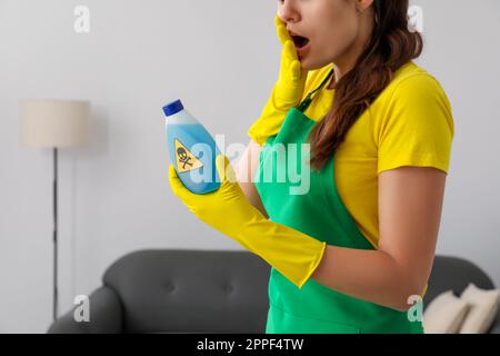 Eine Frau, die auf eine Flasche giftiger Haushaltschemikalien schaut, mit Warnschild, Nahaufnahme Stockfoto