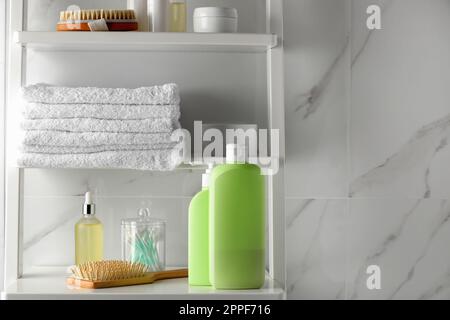 Stapel Handtücher, Bürsten, Shampoo und andere Toilettenartikel auf Regalen nahe der weißen Marmorwand Stockfoto