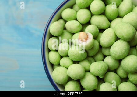 Leckere Wasabi-beschichtete Erdnüsse in der Schüssel auf türkisfarbenem Tisch, Draufsicht Stockfoto