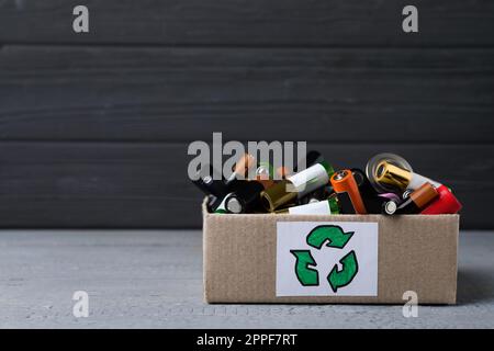 Gebrauchte elektrische Batterien in einem Karton mit Recycling-Symbol auf dem grauen Tisch. Platz für Text Stockfoto