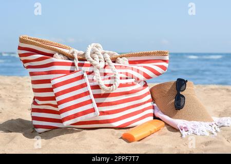 Elegante gestreifte Tasche mit Strandaccessoires auf Sand nahe dem Meer Stockfoto