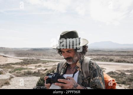 Ein Reisender mit Hut, der sich die Fotos ansieht, die er mit seiner Kamera in einer Wüste macht Stockfoto