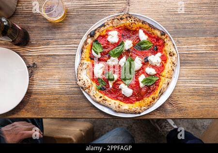 Neapolitanische Margherita Pizza auf einem rustikalen Holztisch in einer traditionellen Pizzeria. Stockfoto