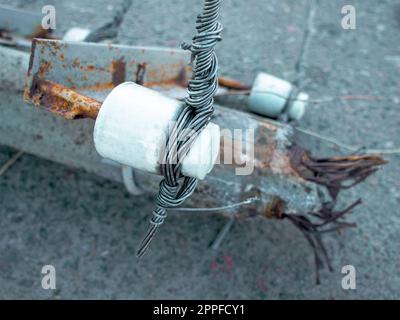 Ein Querisolator auf einem alten rostigen Hochspannungs-Hochspannungsleitungsturm fiel in der Stadt auf Asphalt. Konzept der Elektroenergieindustrie. Stockfoto