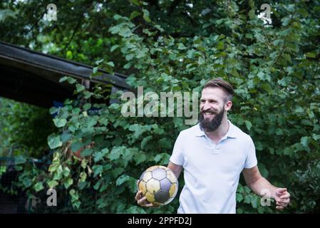 Glücklicher junger Mann, der im Garten, Bayern, Deutschland Fußball spielt Stockfoto