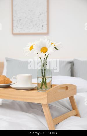 Blumenstrauß mit wunderschönen Gänseblümchen und Frühstück auf einem hölzernen Tablett im Schlafzimmer Stockfoto