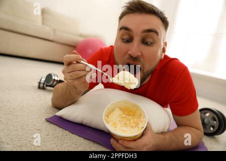 Fauler junger Mann, der Eis isst, anstatt zu Hause zu trainieren Stockfoto