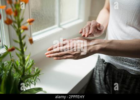 Mittelschnitt einer jungen Frau, die Creme auf ihre Hand aufträgt, München, Bayern Stockfoto