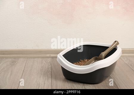 Katzenschale mit biologisch abbaubarem Abfall und Schaufel auf dem Boden nahe der rosafarbenen Wand. Platz für Text Stockfoto