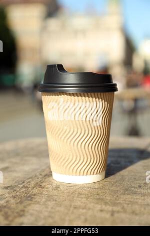 Kaffeetasse zum Mitnehmen aus Karton mit Kunststoffdeckel auf einem Holztisch in der Stadt Stockfoto