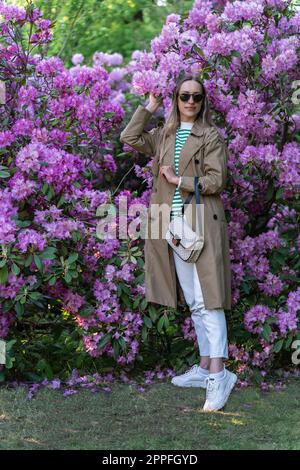 Langhaarige Frau in Sonnenbrille vohle eines üppig blühenden Rhododendron-Busches Stockfoto