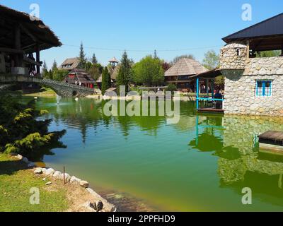 Stanisici, Bijelina, Republika Srpska, Bosnien und Herzegowina 25. April 2021 Ethno-Dorf, Tourismus und Sehenswürdigkeiten. Stein- und Holzgebäude und eine Brücke. Künstlicher Teich mit grünem Wasser Stockfoto