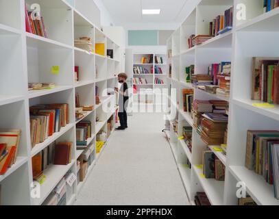 Sremska Mitrovica, Serbien Mai 15 2021 ein 8-jähriger Junge mit Maske und schwarzem T-Shirt steht neben dem Bücherregal in der Bibliothek und liest ein Buch. Schulbildung. Liebe für Literatur und Lesen Stockfoto