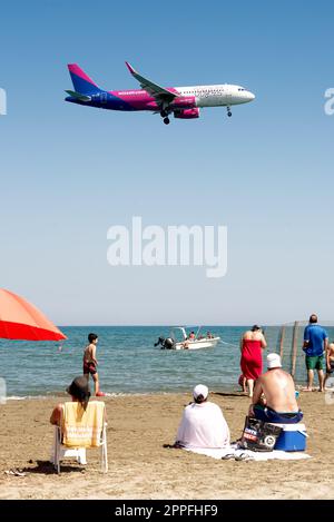 Larnaca, Zypern - 17. September 2022: Menschen, die sich am Strand von Mackenzie ausruhen und Airbus A320-232 der Wizz Air-Fluggesellschaft landen Stockfoto