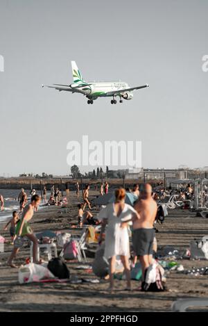 Larnaca, Zypern - 17. September 2022: Menschen, die sich am Strand von Mackenzie ausruhen und den Airbus A319-114 der Cyprus Airways-Fluggesellschaft landen Stockfoto