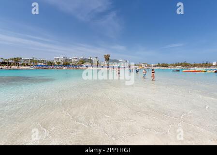 Ayia Napa, Zypern - 07. April 2018: Touristen, die am Strand von Nissi spazieren und baden Stockfoto