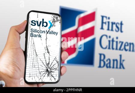 Eine Hand, die ein Telefon mit Silicon Valley Bank Logo auf einem rissigen Bildschirm hält Stockfoto