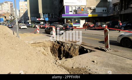 Belgrad, Serbien - 24. Januar 2020. Ein Loch in der Balkanstraße in Belgrad. Männer bei der Arbeit. Zerstörter Asphalt. Ein abgezäunter Ort zum Verlegen oder Reparieren unterirdischer Rohrleitungen. Städtische Infrastruktur. Stockfoto