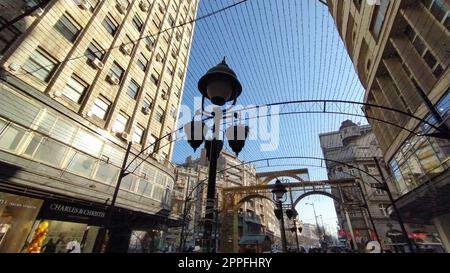 Das Zentrum der Großstadt. Fußgängerzone für Touristen. Ansicht von oben nach unten mit Weitwinkel. Vor dem Hintergrund von Häusern und dem blauen Himmel, eine große Straßenlampe, Drähte und Girlanden. Riesige Gebäude Stockfoto