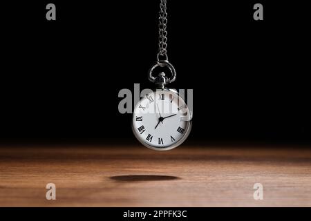 Wunderschöne Taschenuhr im Vintage-Stil mit silberner Kette auf schwarzem Hintergrund über dem Holztisch. Hypnose-Sitzung Stockfoto