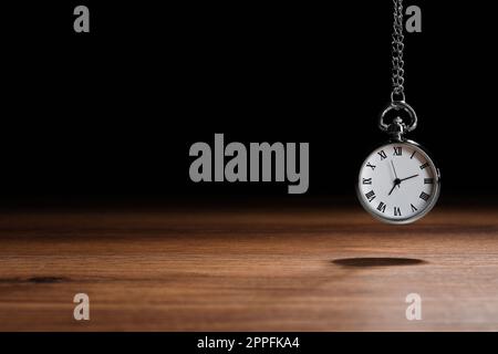 Wunderschöne Taschenuhr im Vintage-Stil mit silberner Kette auf schwarzem Hintergrund über dem Holztisch, Platz für Text. Hypnose-Sitzung Stockfoto