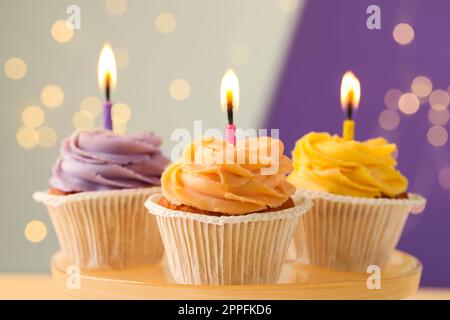 Leckere Geburtstagskuchen mit Kerzen auf dem Stand vor verschwommenem Licht, Nahaufnahme Stockfoto