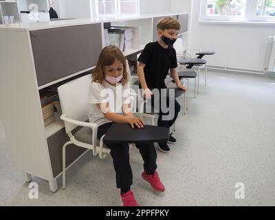 Junge und Mädchen in der Schulbibliothek. Kinder sitzen neben einem Bücherregal. Moderne Schulausrüstung. Drehbare Tische Stockfoto