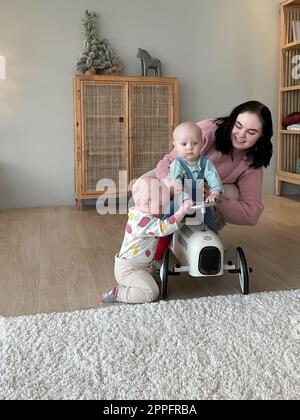 Junge Mutter hält ihre Kinder in einem hölzernen Spielzeugauto sitzen Stockfoto