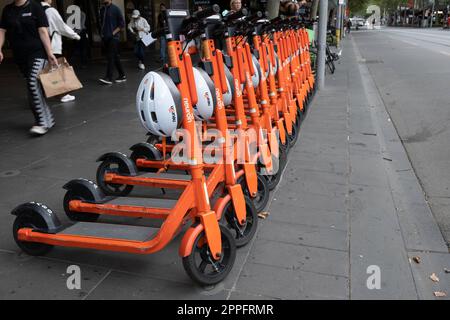 Eine Reihe gemeinsam genutzter Elektrischer Kick-Roller oder E-Steps mit Helmen warten auf Kunden in einer Straße in Melbourne, Victoria, Australien. E-mobil Stockfoto