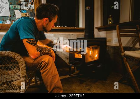 Ein Mann fügt Holz in den alten Ofen des Bauernhauses an der Küste Stockfoto