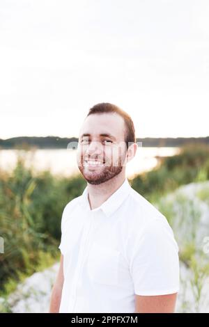 Junger Mann mit Bart im weißen Hemd am Strand im Sommer Stockfoto