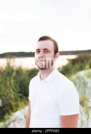 Junger Mann mit Bart im weißen Hemd am Strand im Sommer Stockfoto