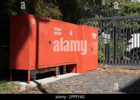 Roter Feuerhydrant und Sprinkler-Druckerhöhungsanlage in einem Metallkasten auf einem Parkplatz Stockfoto