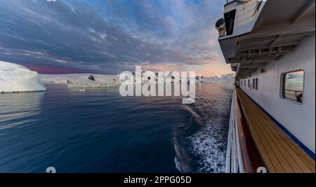 Das Schiff segelt durch die winterliche Cierva Cove - eine tiefe Bucht auf der Westseite der antarktischen Halbinsel, umgeben von der Cierva-Bucht in San MartÃ­n Land - Antarktis, während eines dramatischen Sonnenuntergangs/Abenduntergangs. Stockfoto