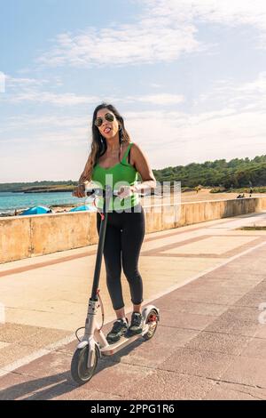 Eine Frau, die mit einem elektrischen Roller fährt, eine glückliche Sommerfahrt im tropischen Insel-Strandresort für den Urlaub. Stadt, Straße und umweltfreundliche Verkehrsmittel, Spaß auf escooter im Urlaub auf mallorca, balearische Insel Stockfoto