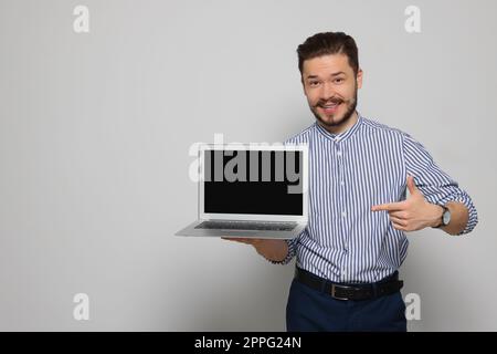 Emotionaler Mann, der auf einen Laptop zeigt, auf hellgrauem Hintergrund. Platz für Text Stockfoto