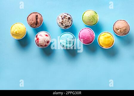 Eissorte. Verschiedene Eis- oder Eissorten auf blauem Hintergrund, Kopierraum. Gefrorener Joghurt in kleinen Pappbechern - gesundes Sommerdessert. Stockfoto