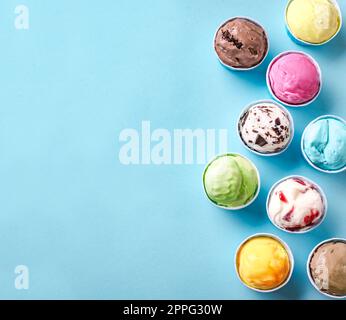 Eissorte. Verschiedene Eis- oder Eissorten auf blauem Hintergrund, Kopierraum. Gefrorener Joghurt in kleinen Pappbechern - gesundes Sommerdessert. Stockfoto